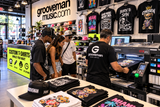 Customers watching custom T-shirt printing on a DTG printer at Grooveman Music in Miami Beach. Personalized graphic tees, while-you-wait printing, and custom streetwear.