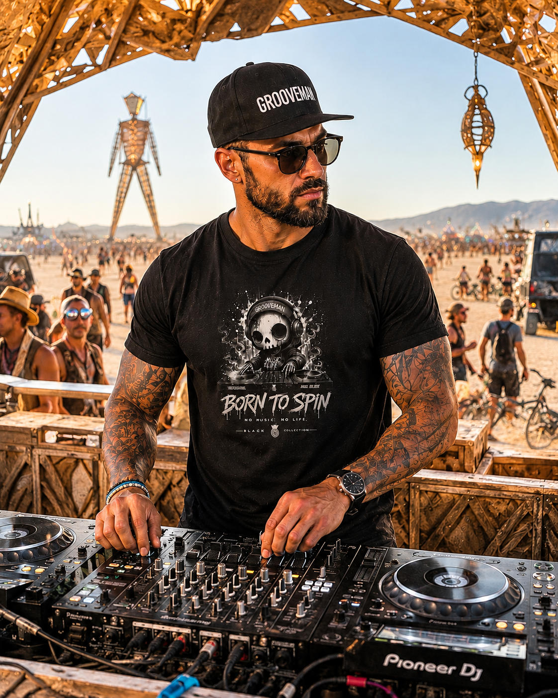 A man at a festival wearing a black t-shirt with a 'Born to Spin' graphic, a black cap with 'GROOVY' on the front, and sunglasses while mixing music on a Pioneer DJ turntable. The background shows a crowded outdoor festival scene with a large robot sculpture under a wooden archway.