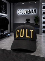 Black cap with 'CULT' in gold on a counter in a store with 'Grooveman' branding.