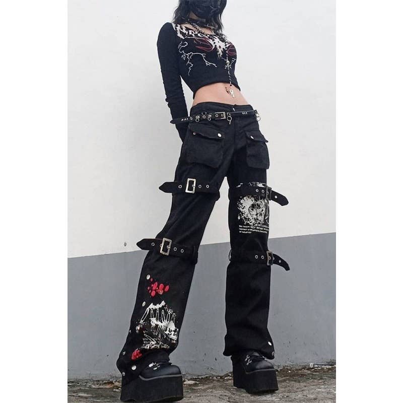 Person wearing black pants with buckles and patches against a plain background