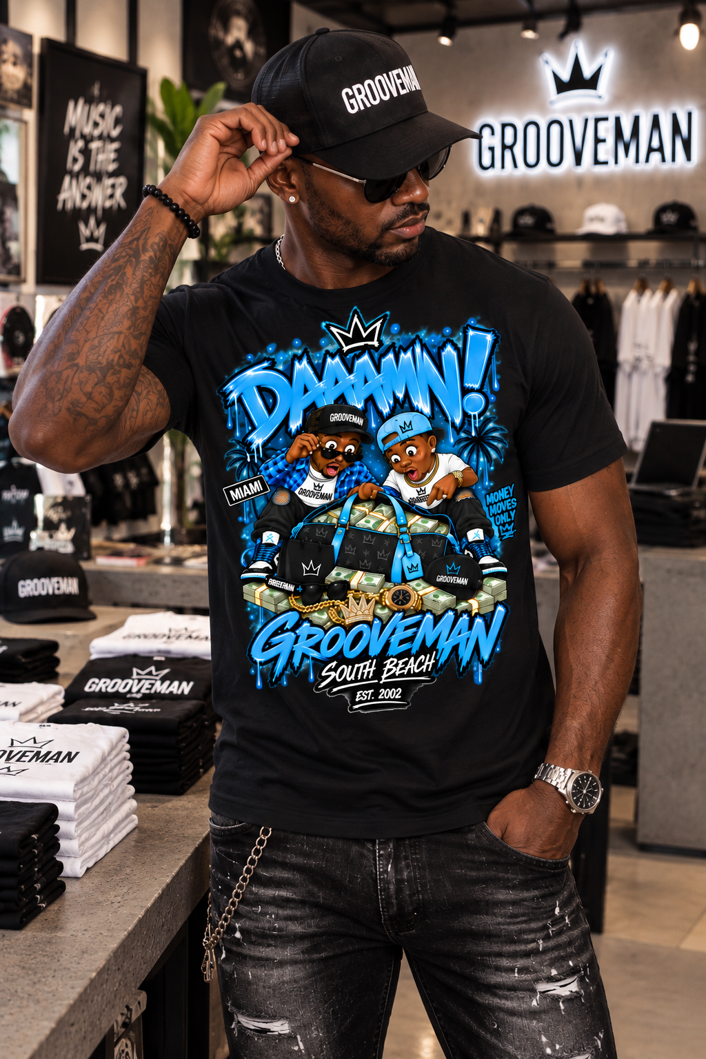 A man wearing a black Grooveman t-shirt with a colorful cartoon graphic of two hip-hop artists, paired with a matching black cap and sunglasses, standing inside a retail store.