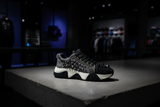 Black glittery sneaker with spikes on a glass surface, blurred store interior in the background