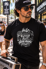 A man wearing a black Groovemain branded t-shirt with a white retro boombox graphic, sunglasses, and a matching cap, carrying a vintage boombox in a sunny outdoor street setting.
