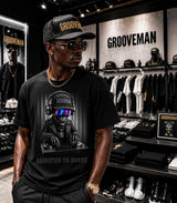 A man wearing a black Grooveman t-shirt with a DJ skull graphic, standing inside a retail store. The shirt features a graphic of a DJ skull wearing headphones and sunglasses with the text 'GROOVEMAN' and 'ADDICTED TO HOUSE'.