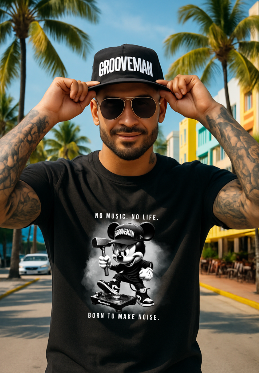 Man wearing a black t-shirt with 'Grooveman' design and a cap, standing outdoors with palm trees in the background.