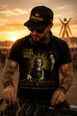 DJ at sunset with tattoos and a 'Grooveman' cap, wearing a t-shirt with a graphic design.