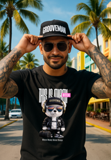 Man wearing a black t-shirt with a graphic design and 'Grooveman' cap in a tropical setting.