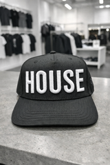 Black cap with 'HOUSE' text on a store shelf background