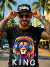 Man wearing a black t-shirt with a colorful lion graphic and 'King' text, sunglasses, and a 'Grooveman' cap in a tropical setting.