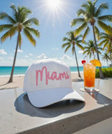 White cap with 'Miami' in pink on a beach setting with palm trees and a cocktail.