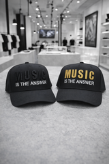 Two black caps with 'Music is the Answer' text on a gray surface, with a store interior in the background.