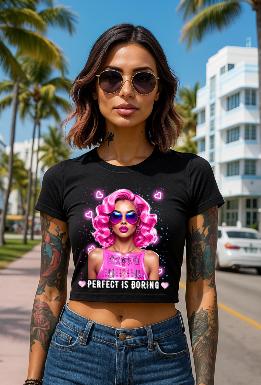 Woman wearing a black t-shirt with a graphic design and text, standing on a street with palm trees and buildings in the background.