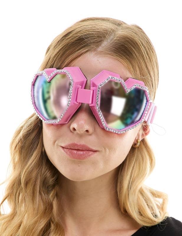 Person wearing pink goggles with heart-shaped lenses on a white background