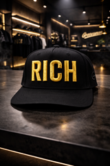 Black cap with 'RICH' in gold on a reflective surface in a store setting
