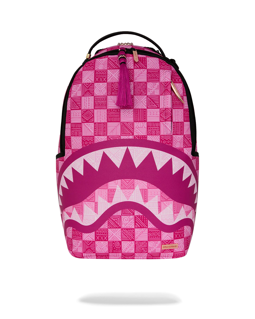A pink and white patterned backpack with a shark mouth graphic on the front, featuring a top handle, black zippers, and a small gold brand plaque.