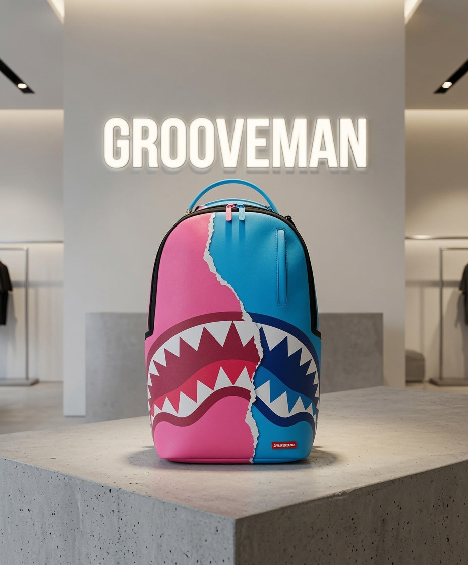 A colorful Grooveman backpack with a pink and blue shark-face graphic, displayed on a concrete pedestal inside a modern retail store.