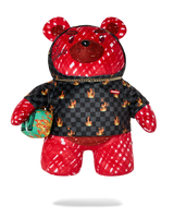 A red and black patterned teddy bear plush toy wearing a black checkered jacket with flame motifs, red patterned pants, and holding a green patterned pouch, shown against a plain white background.