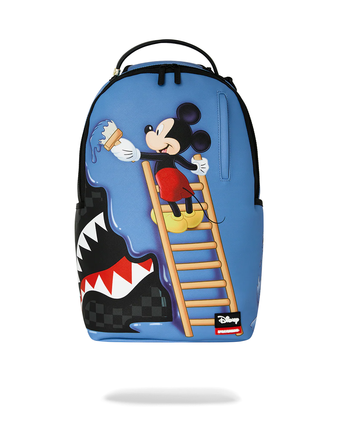A blue backpack featuring a Mickey Mouse climbing a ladder to drink from a water droplet, with a shark mouth design on the lower left side and a small Disney logo patch near the bottom right.