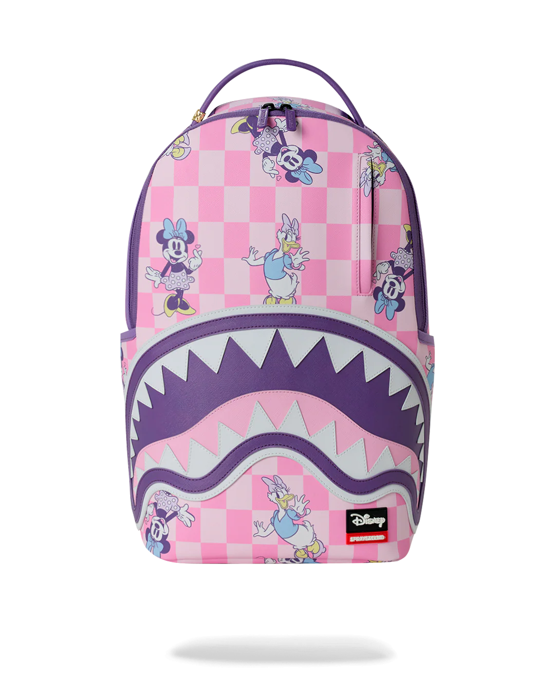 A pink and purple backpack featuring a checkerboard pattern with cartoon characters, a large shark-mouth graphic across the lower half, and a visible Disney logo patch near the bottom right.