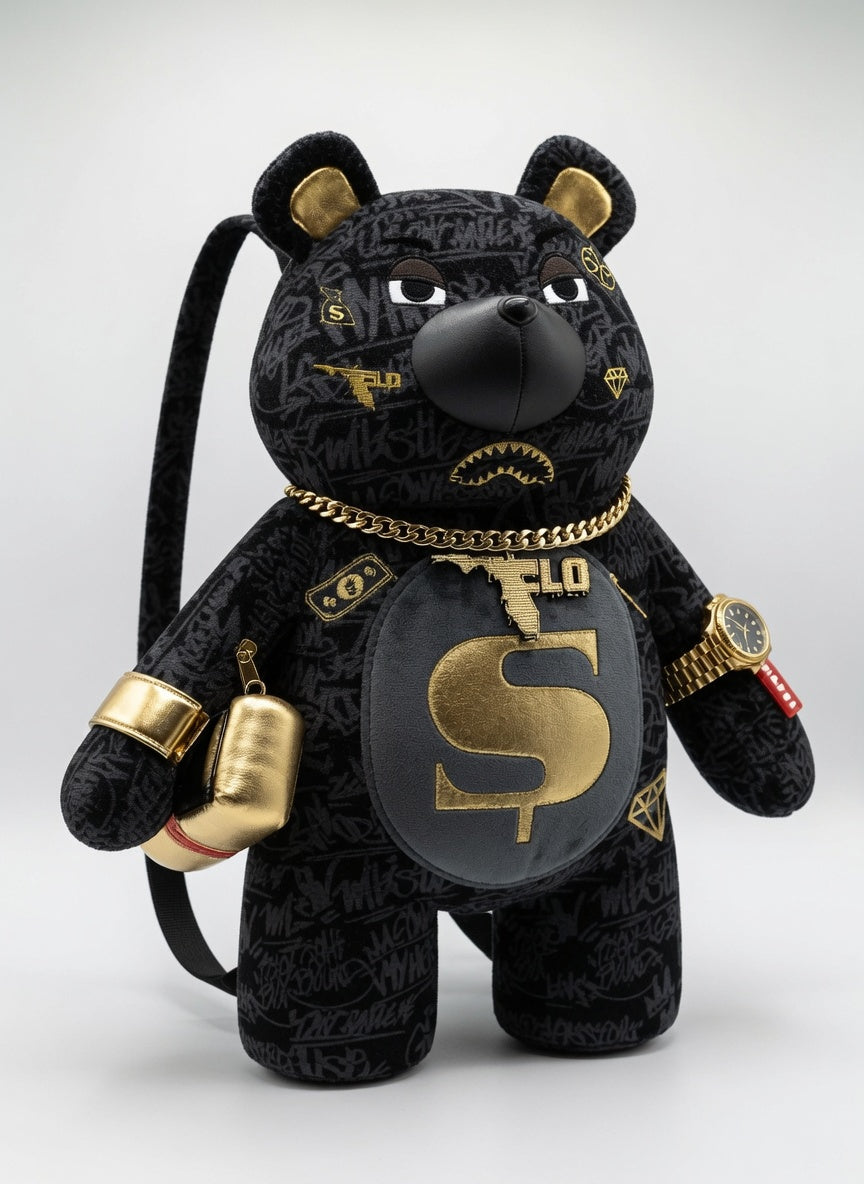 A black plush bear accessory with gold and gray graffiti-style details, featuring a large gold dollar sign on its chest, a gold chain necklace, boxing gloves, and a watch, set against a light gray background.