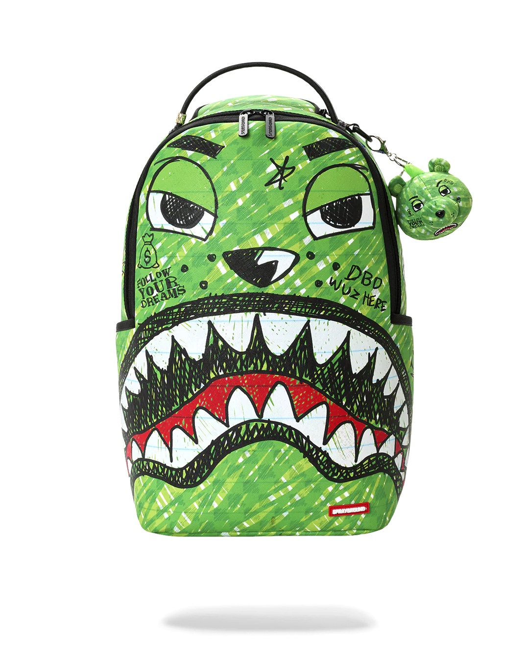 A green Spraycraft backpack featuring a stylized shark-face graphic with black, white, and red details, a top handle, and a small matching green keychain charm.