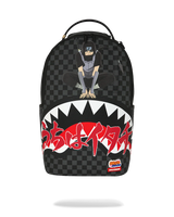 A black and dark gray checkered backpack featuring a graphic of a ninja sitting on the upper front, a large white shark mouth with red Japanese text across the lower half, and a small Sprayground logo patch near the bottom right.