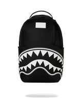 A black backpack featuring a bold white shark mouth graphic with sharp teeth across the lower front, shown on a clean white background.