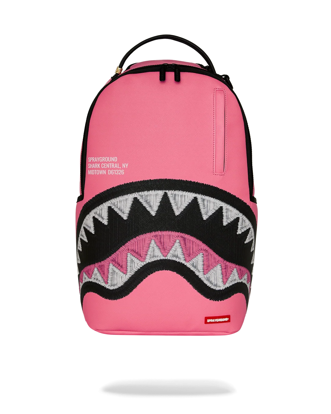 A pink Sprayground Shark backpack with a black and white shark mouth graphic on the front, featuring a top carry handle and a vertical zippered pocket on the upper right side.