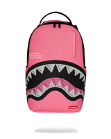 A pink Sprayground Shark backpack with a black and white shark mouth graphic on the front, featuring a top carry handle and a vertical zippered pocket on the upper right side.