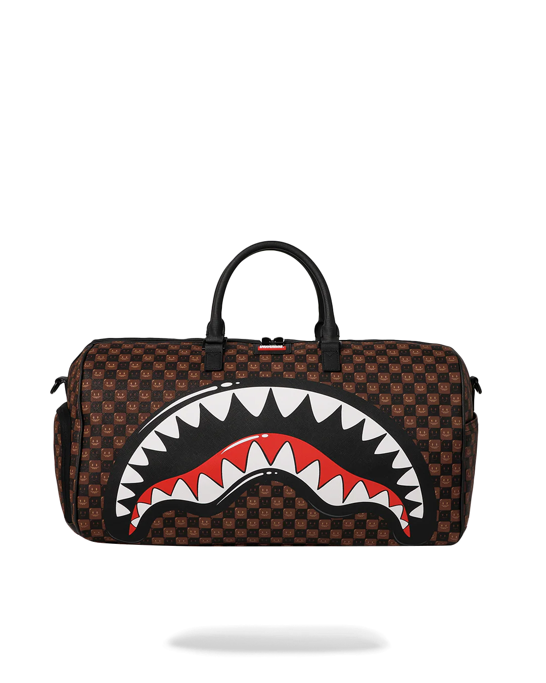 A brown checkered duffel bag featuring a large shark mouth graphic on the front with white teeth, a red interior, and black outlines. The bag has black top handles and is shown against a plain white background.