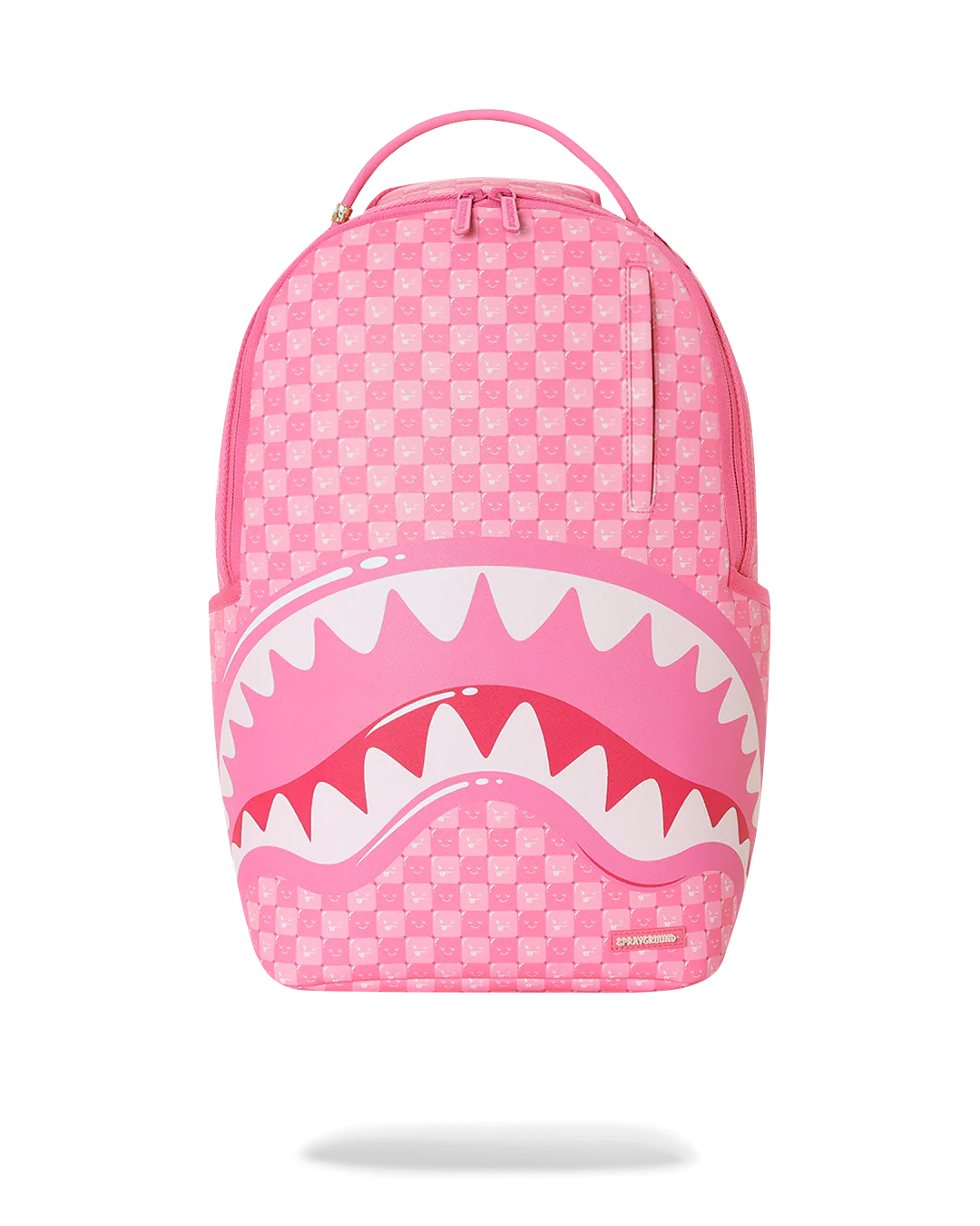 A pink Shark Day backpack featuring a pink and white checkerboard pattern, a large shark mouth graphic with white teeth across the lower front, and a top carry handle, shown on a white background with a soft shadow underneath.
