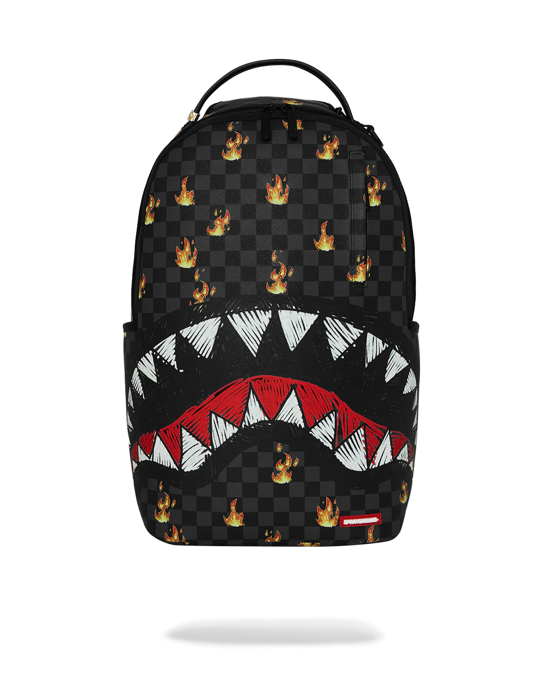 A Sprayground Shark backpack in black checkered canvas with a graphic of a shark mouth showing white and red teeth, and small orange and yellow fire logos scattered across the surface.