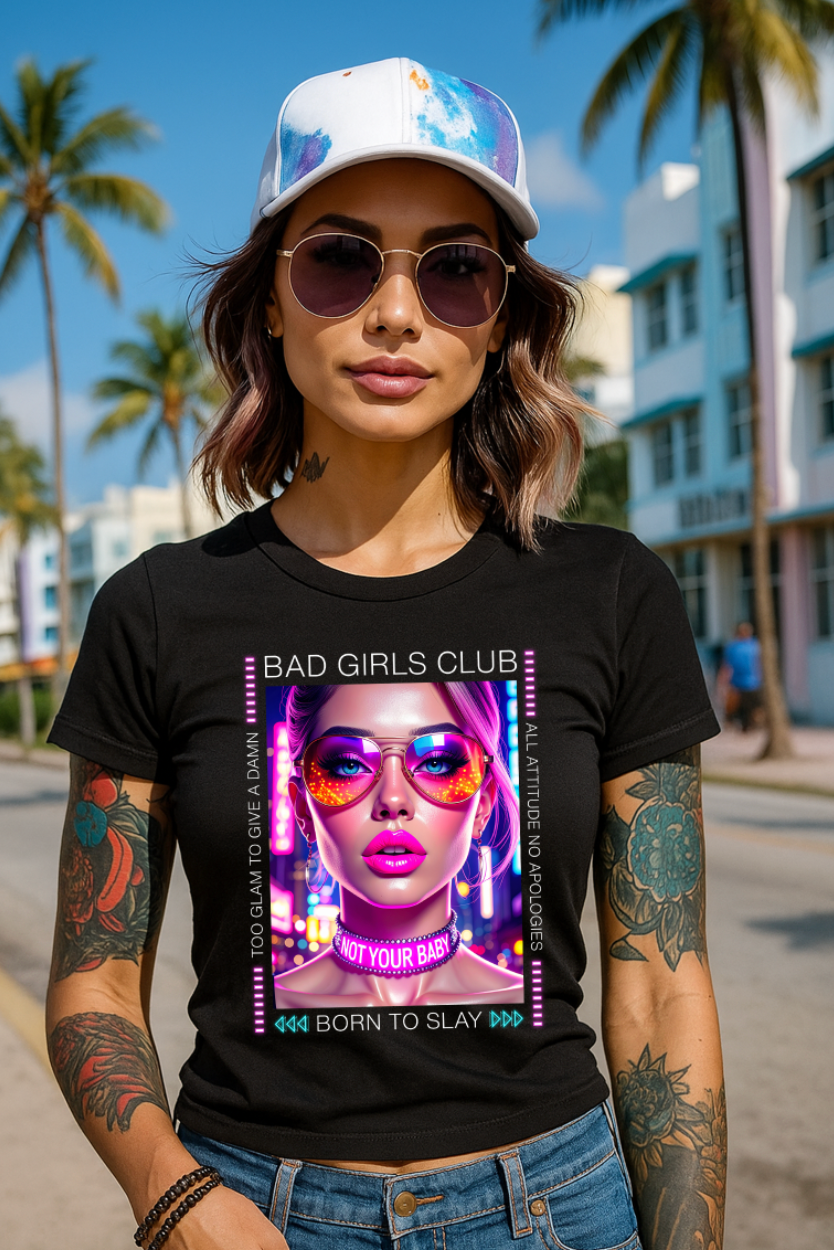Woman wearing a black t-shirt with 'Bad Girls Club' design, sunglasses, and cap in a palm tree-lined street.